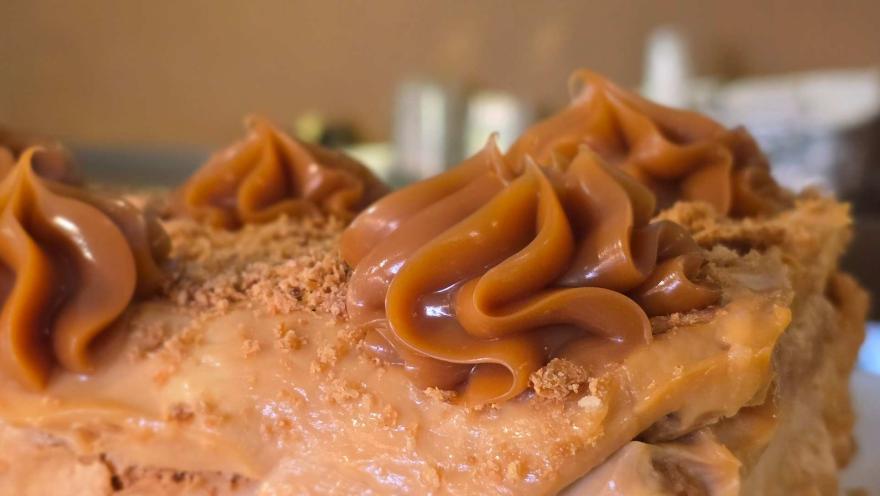 Primer plano de pastel decorado con rosetones de dulce de leche o arequipe y migas de galleta espolvoreadas. 