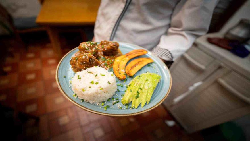 Primer plano de plato servido con albóndigas en salsa, arroz blanco, tajadas de plátano maduro y aguacate.