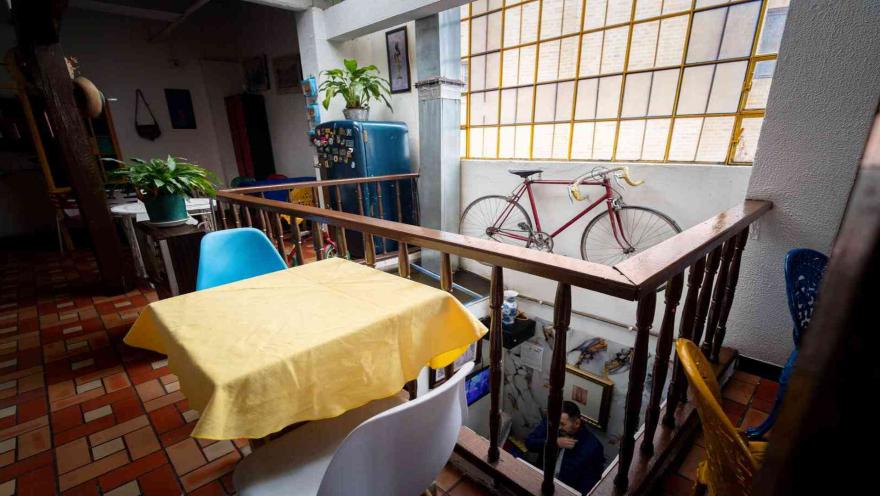  Área con una pequeña mesa, barandilla de madera y una bicicleta de carretera roja colgada frente a una ventana con rejas.