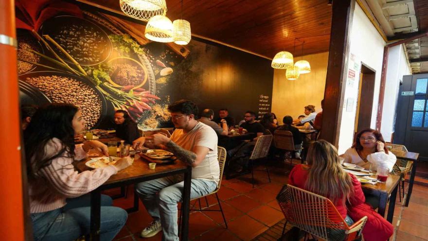 Personas cenando en mesa del restaurante frente a mural decorativo de especias e iluminación cálida. 