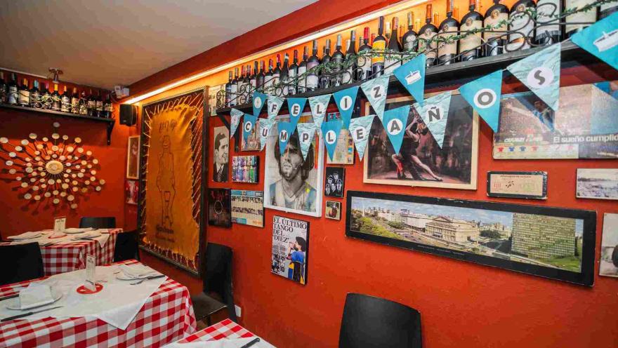 Pared roja decorada con imágenes de tango, fotos de Maradona, banderines de Feliz Cumpleaños y estante de vinos.