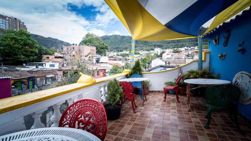 Terraza con toldo de colores y mesas de hierro forjado. Ofrece una vista amplia de la ciudad y las montañas circundantes.