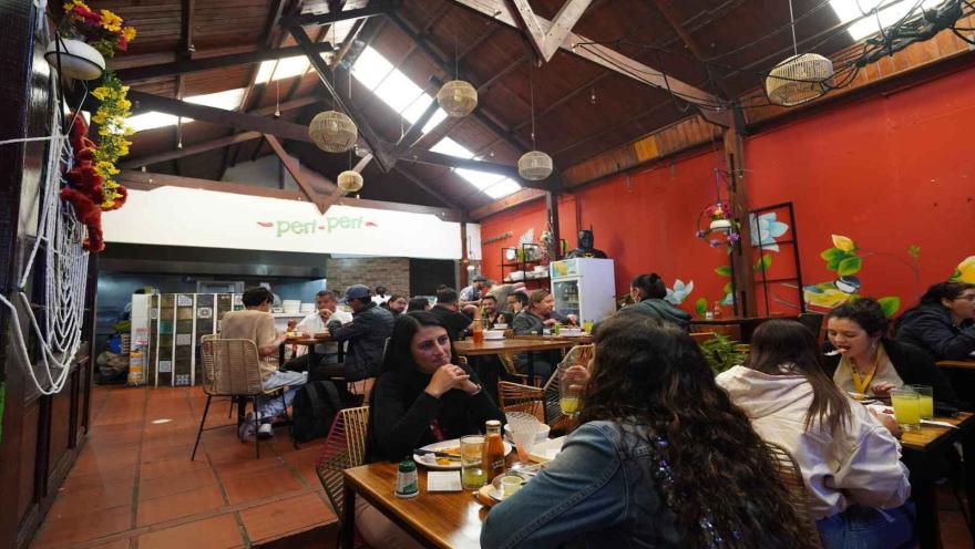 Vista en perspectiva del interior de Peri Peri con comensales sentados bajo la estructura de madera. 