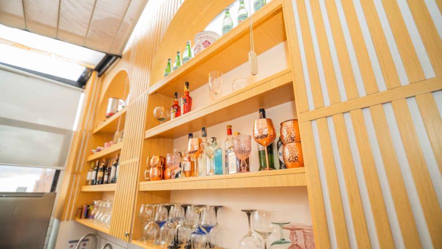  Contrapicado de la repisa de madera en forma de arco con botellas de whisky, aperitivos, tazas de cobre y copas.