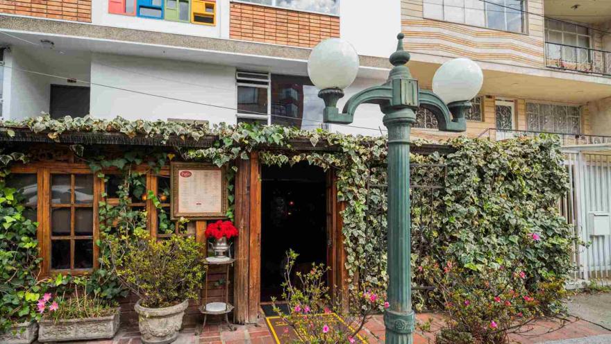 Fachada rústica rodeada de enredaderas con una farola clásica de hierro y flores de colores en la entrada.