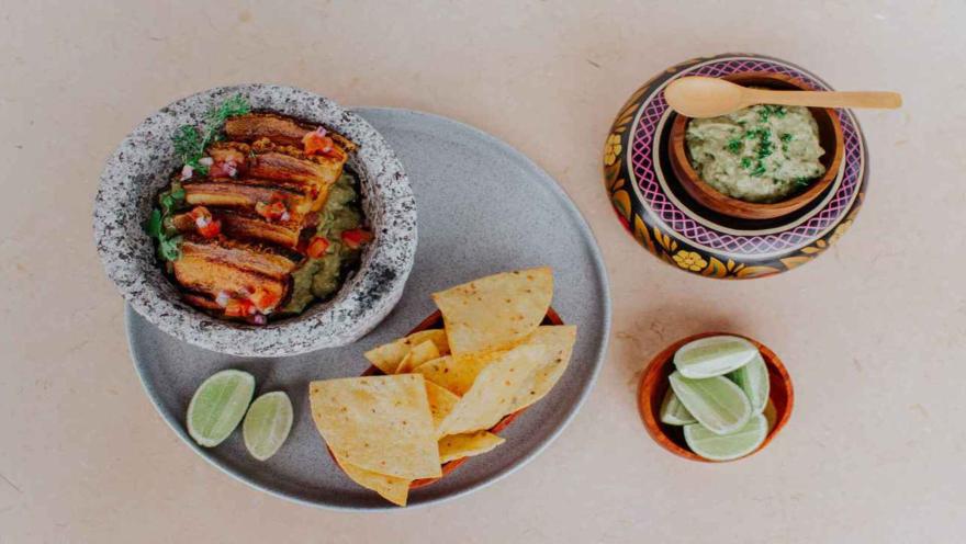 Plato con chicharrón sobre guacamole, acompañado de totopos, limones y una salsa cremosa.