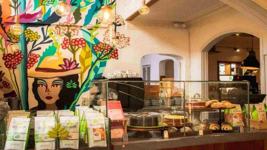  Mostrador con bolsas de café, vitrina de repostería y un colorido mural ilustrado con el rostro de una mujer. 