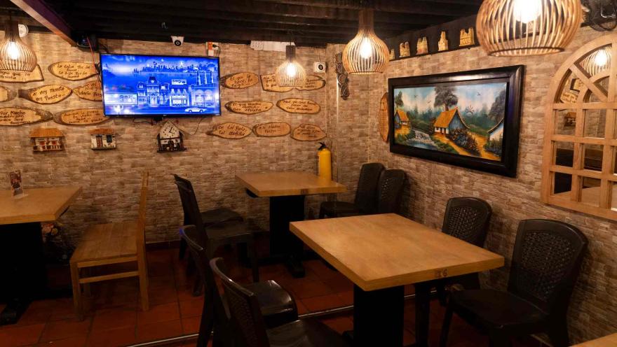 Comedor con mesas de madera, paredes tipo piedra, réplicas de fachadas y un cuadro de paisaje rural. 