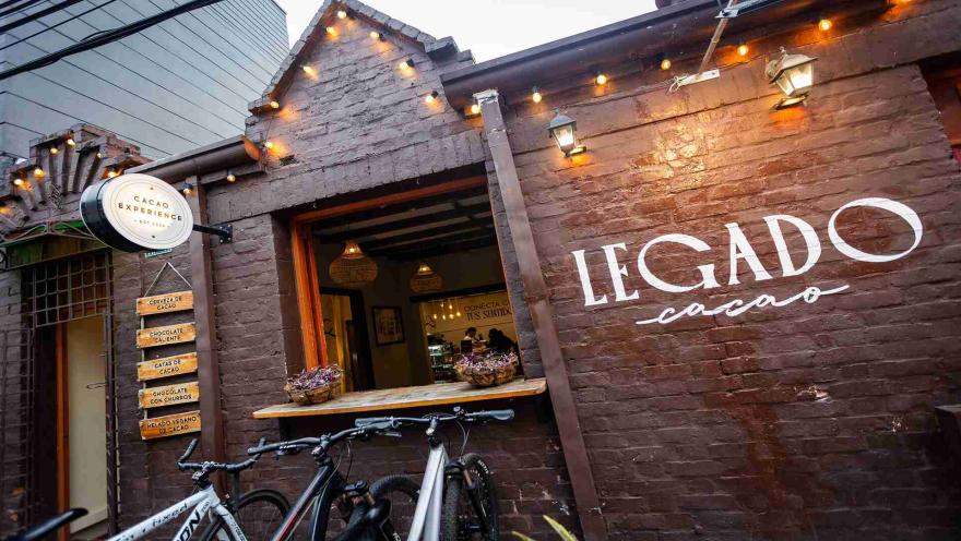 Fachada de ladrillo de Legado Cacao de día con bicicletas parqueadas y letrero en la pared exterior. 
