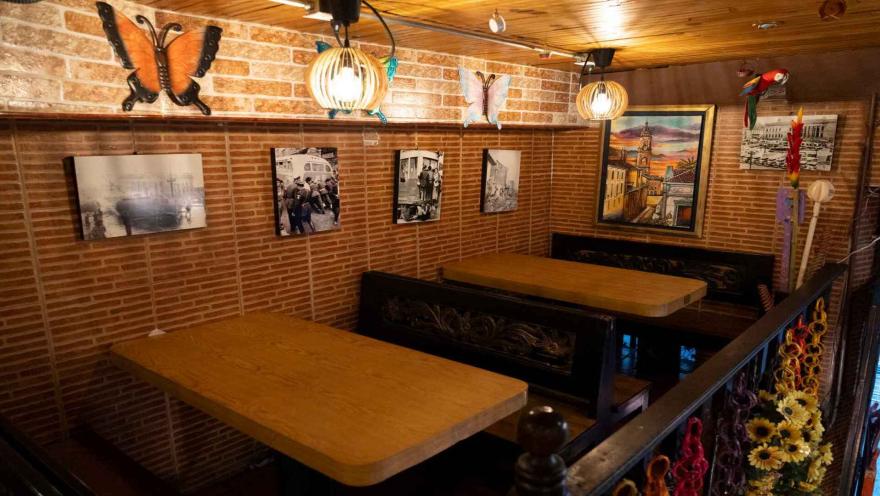  Zona superior del comedor con mesas de madera, pared de ladrillo con fotografías antiguas y adornos de mariposas. 