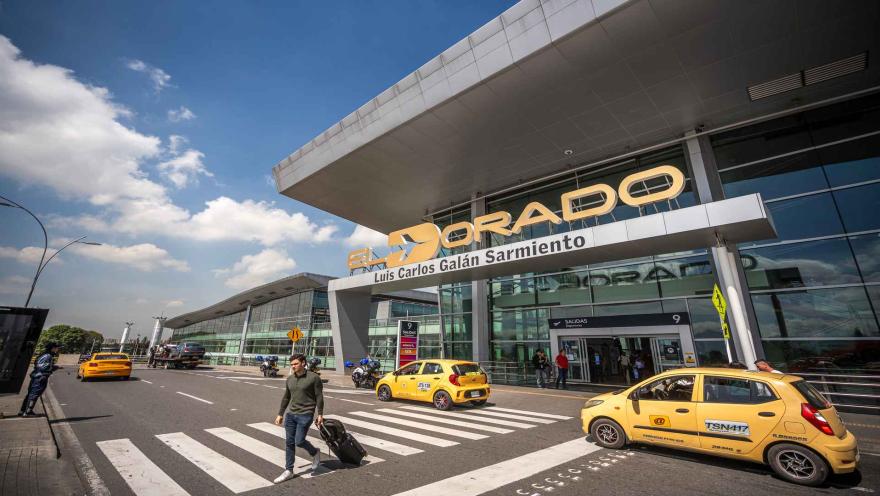 Entrada principal del Aeropuerto El Dorado de Bogotá, con viajeros, taxis y la fachada de la terminal aérea.