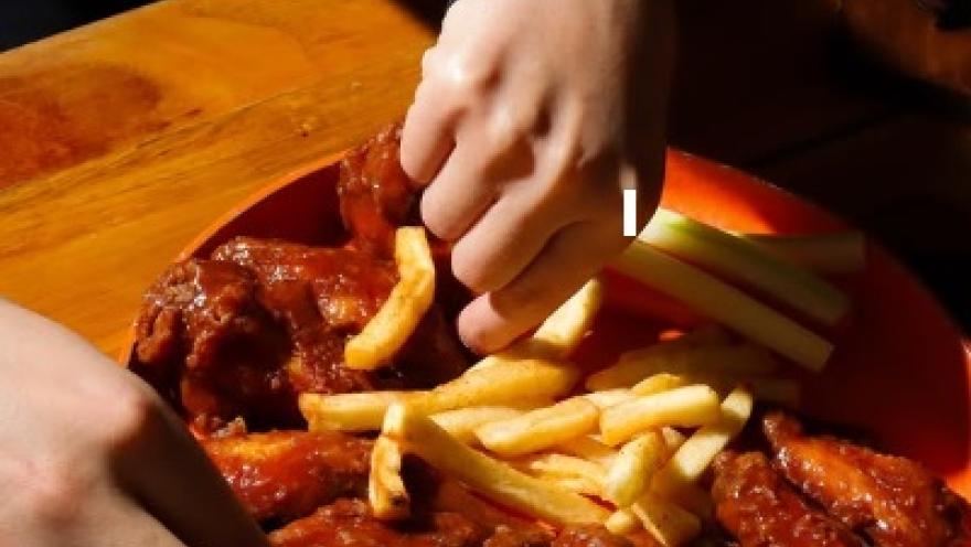 Alitas de pollo bañadas en salsa, acompañadas de papas fritas y vegetales.
