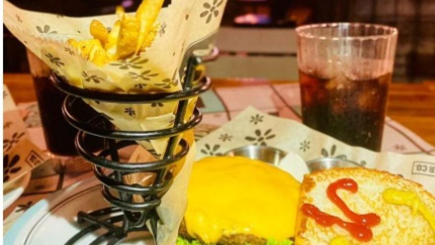 Hamburguesa con queso, lechuga y salsa, acompañada de papas fritas y una bebida gaseosa.