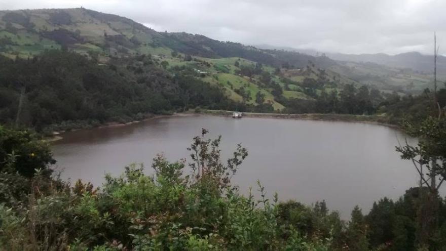 Laguna rodeada de montañas, árboles y vegetación rural, en un paisaje natural de ambiente tranquilo.