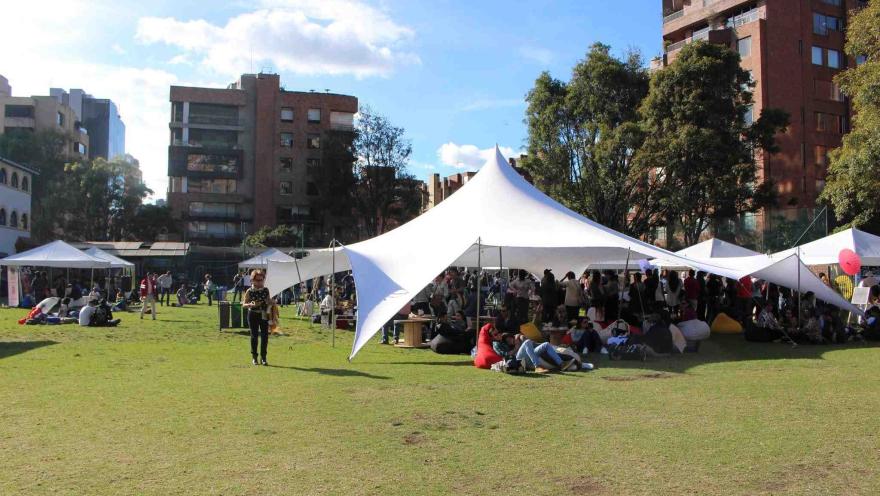 Personas disfrutando de un evento al aire libre en un parque, bajo grandes carpas blancas.
