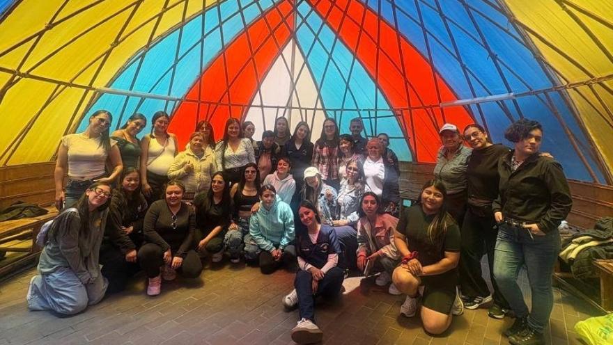  Grupo de participantes posa en un espacio comunitario decorado con una colorida estructura artesanal.