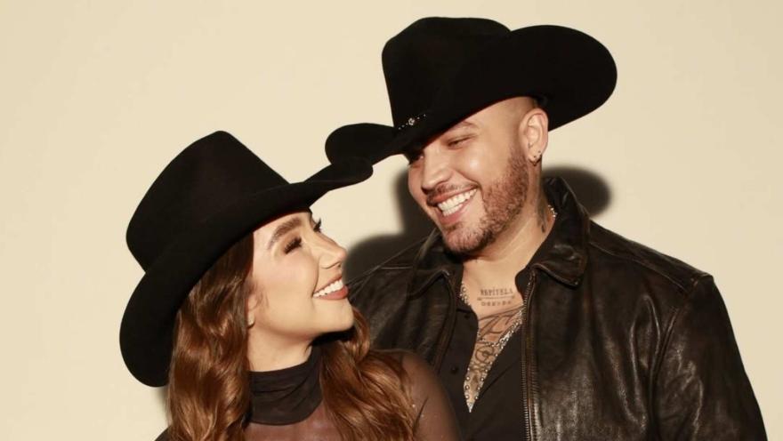 Los cantantes de música popular Paola Jara y Jessi Uribe, sonrientes con sombreros negros de estilo vaquero.