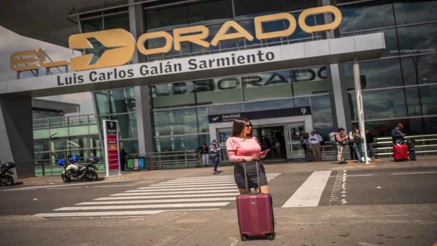 Mujer con una maleta frente a la entrada del Aeropuerto El Dorado, junto al acceso de salidas de la terminal aérea.