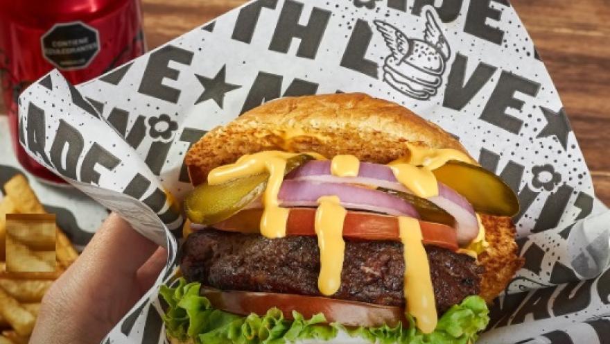 Hamburguesa artesanal con carne, queso, lechuga, tomate, cebolla y pepinillos, servida en pan con semillas.