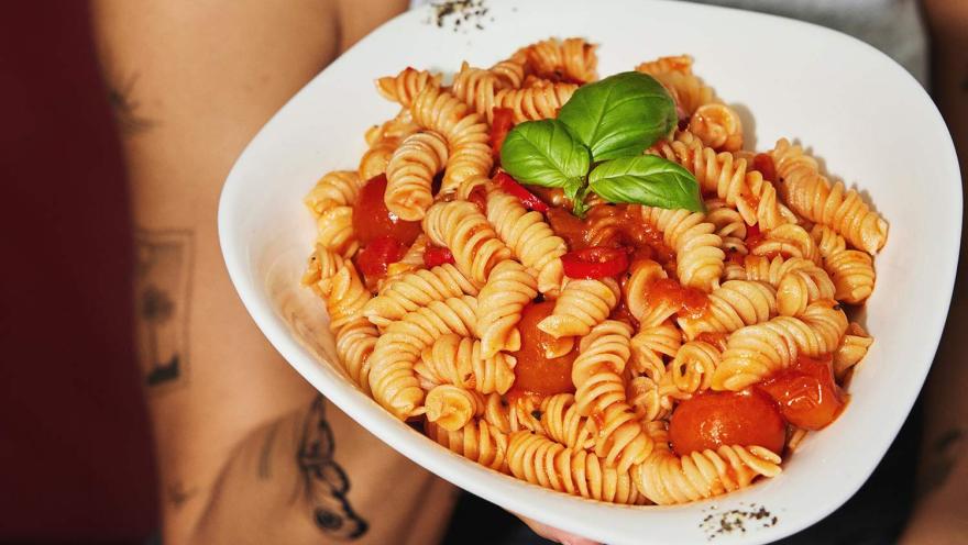  Pasta fusilli con salsa de tomate, tomates cherry y hojas frescas de albahaca, servida en un plato blanco.