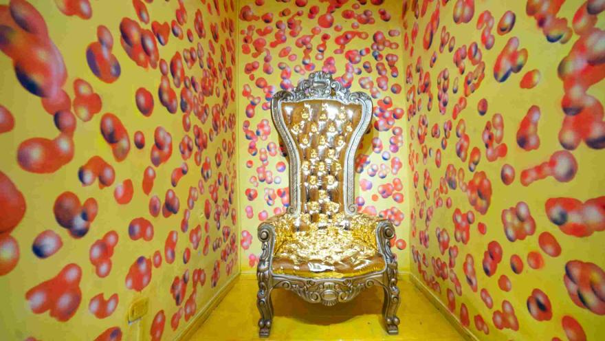Salón amarillo del Museo de la Selfie en Bogotá, con paredes y piso decorados con numerosas formas circulares de colores. En el centro se encuentra un llamativo trono dorado con detalles ornamentales, dispuesto como escenario para fotografías.