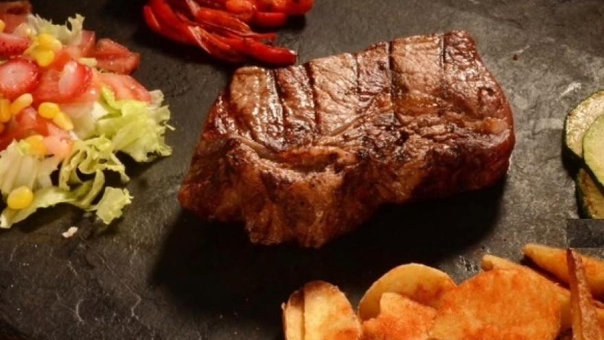 Corte de carne a la parrilla acompañado de ensalada, papas y vegetales.