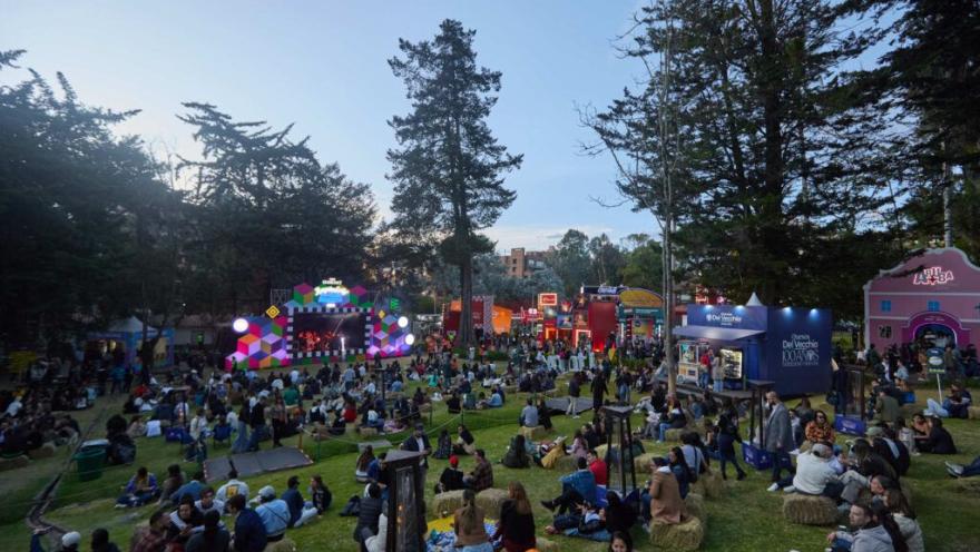 Festival gastronómico nocturno con música en vivo, restaurantes y público reunido en un parque.