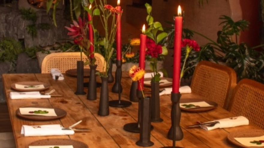 Mesa de restaurante decorada con velas, flores y vajilla, en un ambiente cálido y sofisticado.