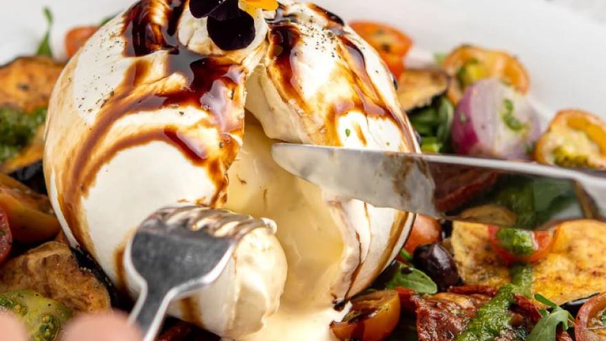 Burrata cremosa bañada con reducción de balsámico, acompañada de vegetales y tomates.
