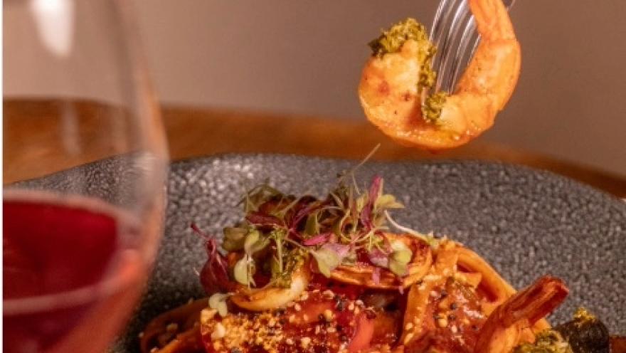 Plato de mariscos con camarones, vegetales y hierbas frescas, acompañado de una copa de vino.