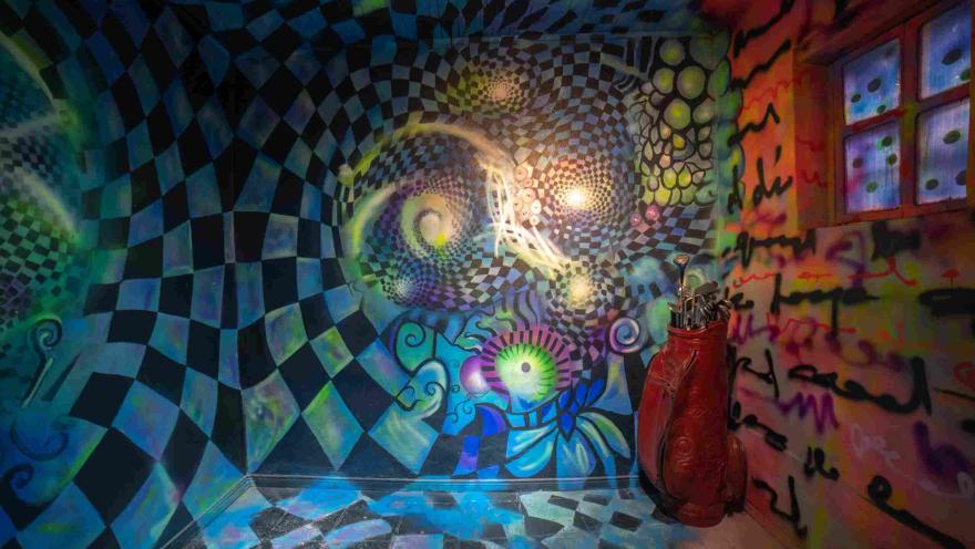 Espacio inmersivo del Museo de la Selfie en Bogotá, decorado con murales psicodélicos en tonos azules, verdes y morados. Las paredes y el piso presentan patrones geométricos que crean un efecto visual de movimiento, acompañado de elementos decorativos y luces de colores.