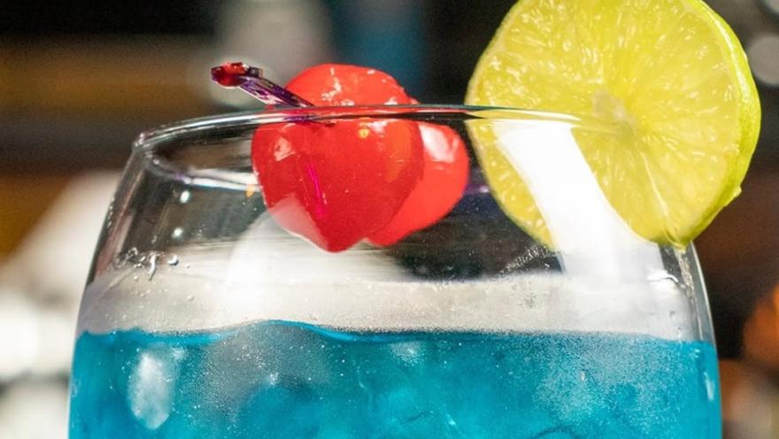 Cóctel azul servido con hielo, cereza y rodaja de limón.