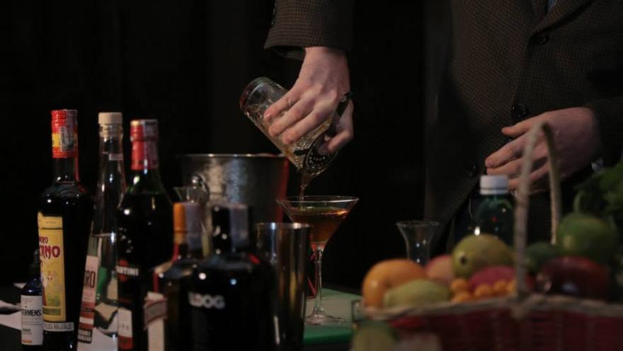  Persona preparando un cóctel con bebidas, frutas y utensilios de bar.