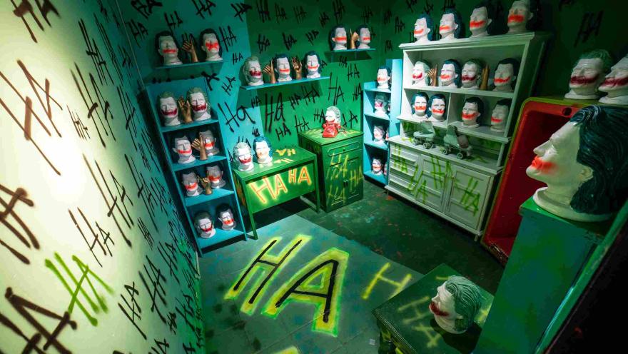 Sala temática del Museo de la Selfie en Bogotá, ambientada en tonos verdes y decorada con numerosas máscaras y cabezas de maniquí con maquillaje inspirado en el personaje del Joker. Las paredes, muebles y piso están cubiertos con grafitis que repiten expresiones de risa, creando un escenario teatral y llamativo para fotografías.