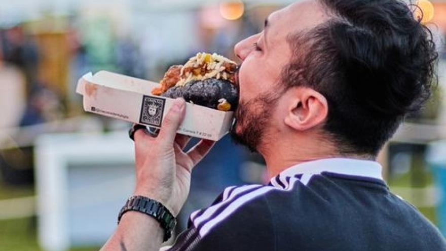  Hombre disfrutando de una hamburguesa durante un festival gastronómico al aire libre.