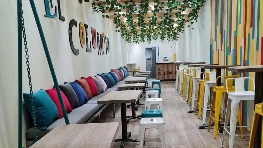 Salón de El Columpio con mesas, sillas coloridas y decoración vegetal.