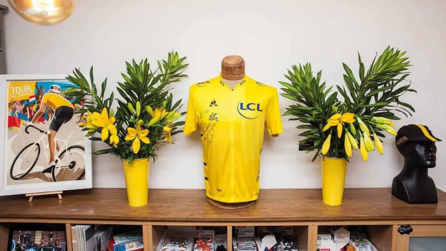  Jersey amarilla del Tour de Francia exhibida en Moovil, acompañada de flores, ilustraciones y recuerdos del ciclismo.