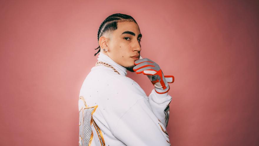 Omar Courtz, de perfil con trenzas, chaqueta blanca y un guante deportivo, posa con la mano en el mentón.