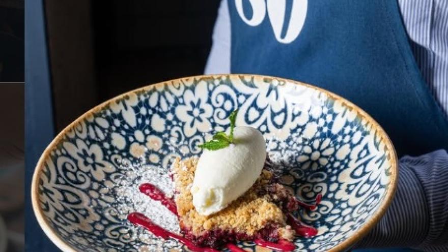 Postre artesanal de 80 Sillas, servido en un plato decorativo, con crema, frutos rojos y crumble.