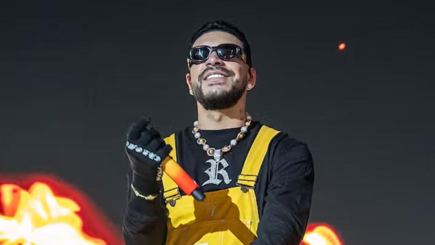 El cantante urbano Ryan Castro con gafas oscuras, micrófono y overol amarillo en un escenario iluminado.