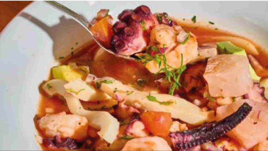 Cuchara levantando trozos de pulpo y pescado en salsa de ceviche sobre plato hondo con mariscos variados.