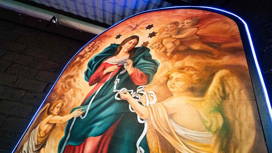 Pintura religiosa con arco iluminado que muestra a la Virgen Maria desatando nudos con ayuda de ángeles.