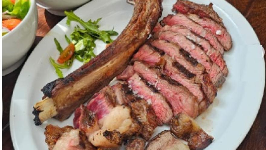 Corte de res a la parrilla en láminas, acompañado de ensalada fresca y vegetales.