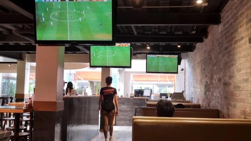 Interior de Hooters Zona T con pantallas que transmiten un partido de fútbol, mesas y cómodas zonas para disfrutar del ambiente deportivo.