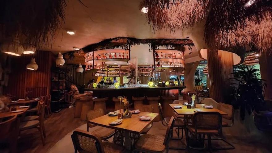 Interior de El Mono Bandido con barra central, iluminación cálida, decoración tropical y mesas para compartir.