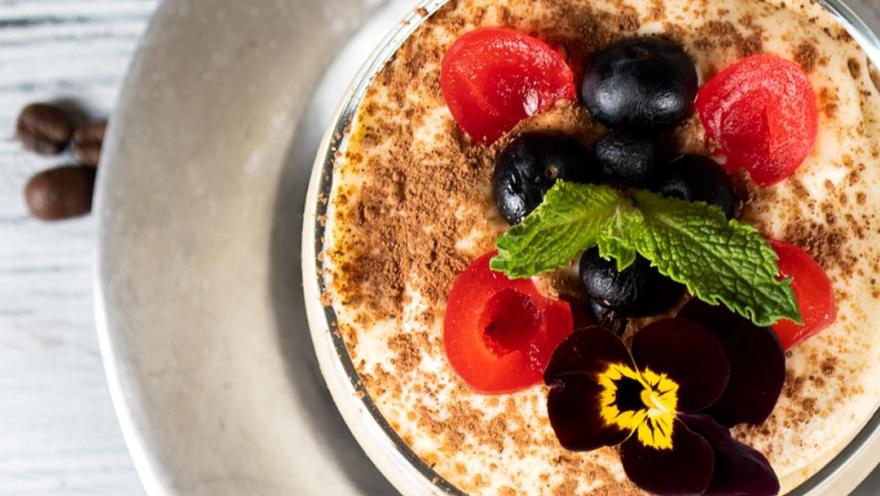 Postre cremoso tipo tiramisú, decorado con frutos rojos, arándanos y menta fresca.
