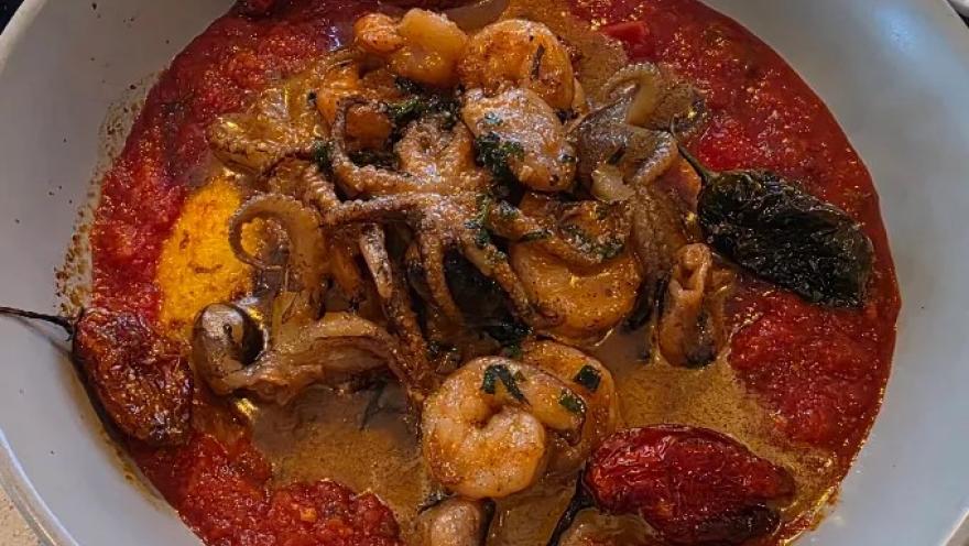 Preparación de mariscos y vegetales salteados, acompañados de tomates y una salsa de textura cremosa.