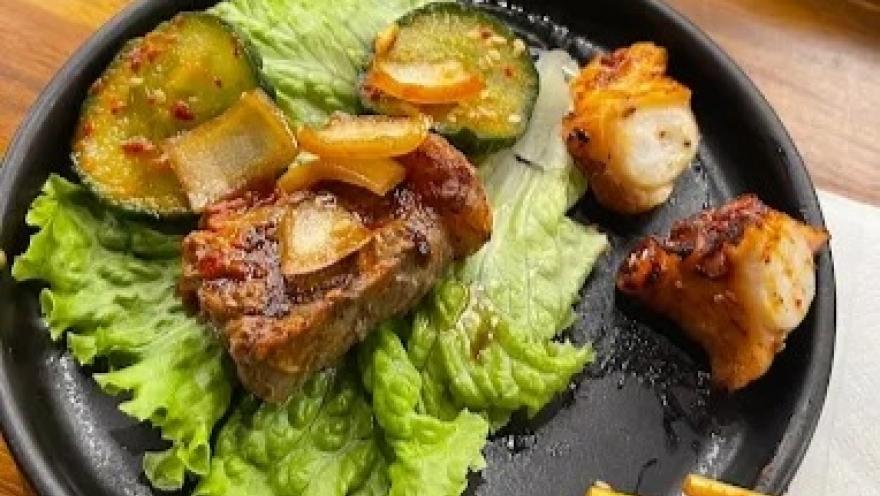 Selección de carnes a la parrilla acompañadas de lechuga y vegetales, servidas en un plato negro.