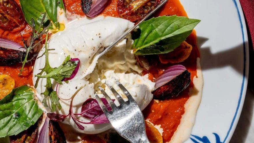 Burrata cremosa con salsa de tomate, tomates asados, cebolla y hojas frescas.