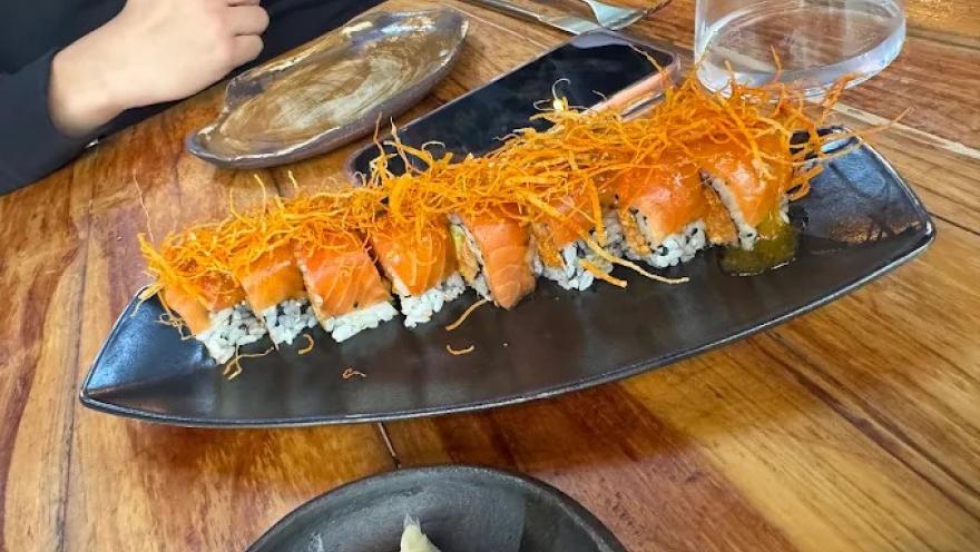 Roll de sushi con salmón, arroz y cobertura crujiente, servido en un plato negro.